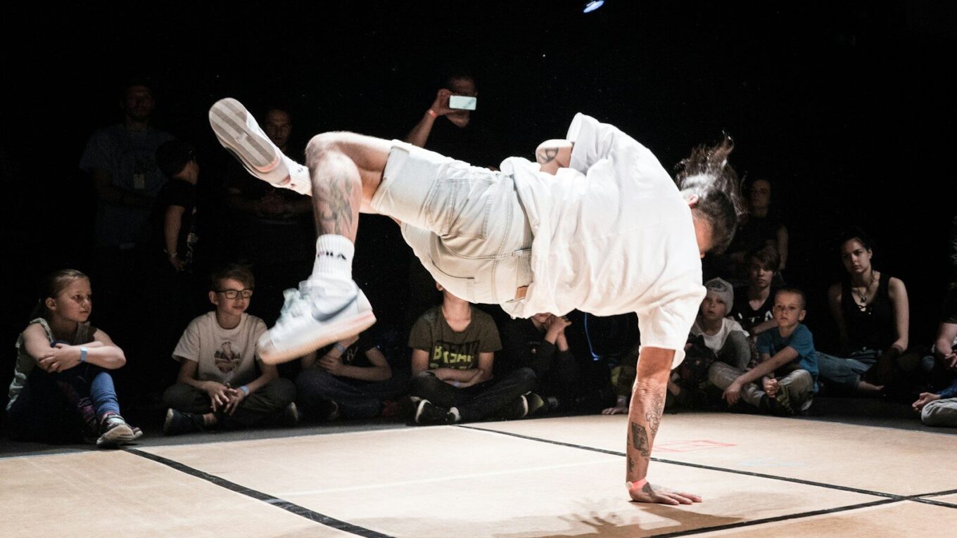 man in white dress shirt and white pants jumping on brown wooden floor